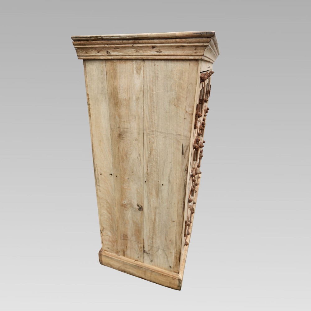 A light natural teak two-door storage cupboard featuring heavy iron straps, studs, and ring handles. View VII