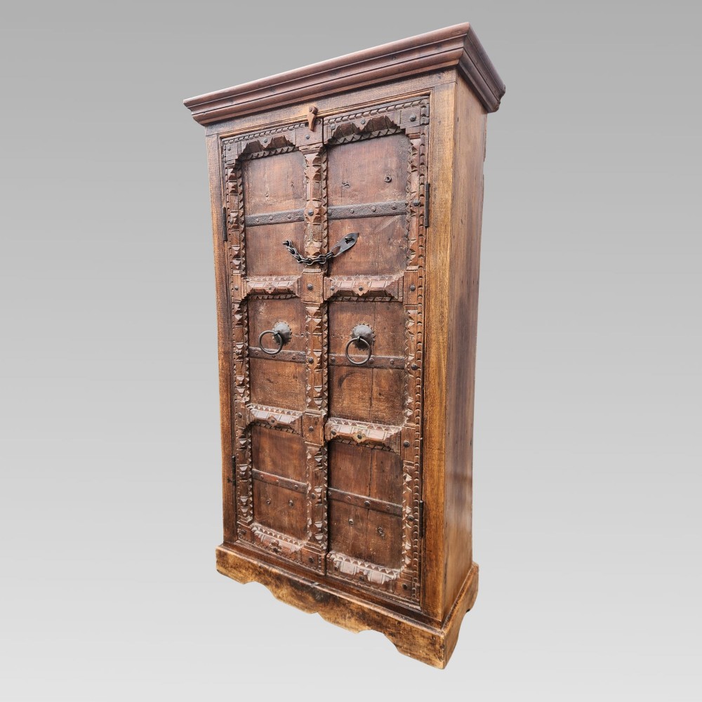 A tall antique Indian cupboard constructed from warm brown reclaimed teak wood with carved frame borders, panelled doors, and rustic iron ring handles. View III