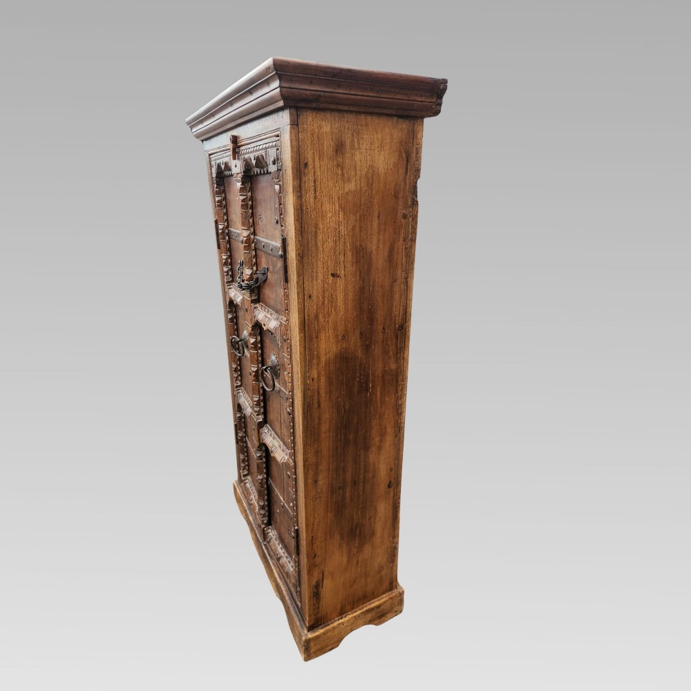 A tall antique Indian cupboard constructed from warm brown reclaimed teak wood with carved frame borders, panelled doors, and rustic iron ring handles. View IV