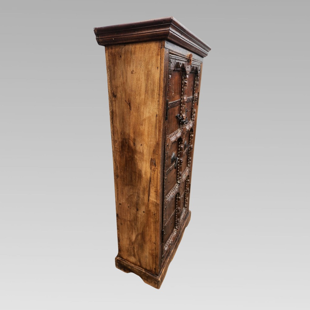 A tall antique Indian cupboard constructed from warm brown reclaimed teak wood with carved frame borders, panelled doors, and rustic iron ring handles. View V