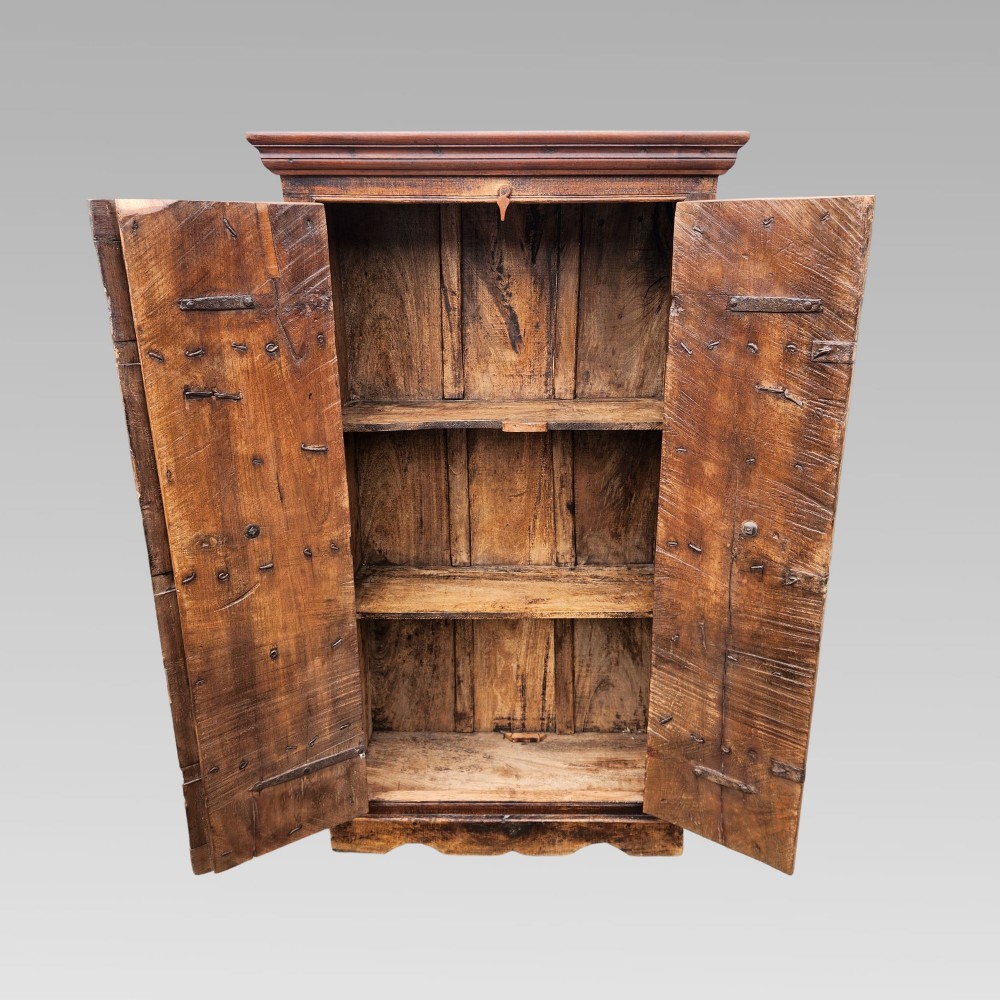 A tall antique Indian cupboard constructed from warm brown reclaimed teak wood with carved frame borders, panelled doors, and rustic iron ring handles. View VI