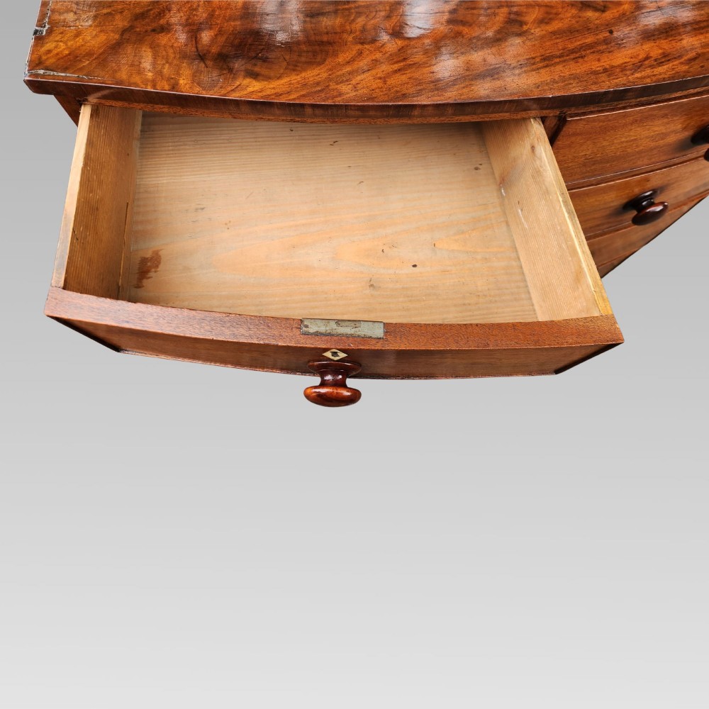 A Victorian mahogany bow-front chest of drawers featuring two short drawers over three long drawers with dark turned handles and turned feet. View X
