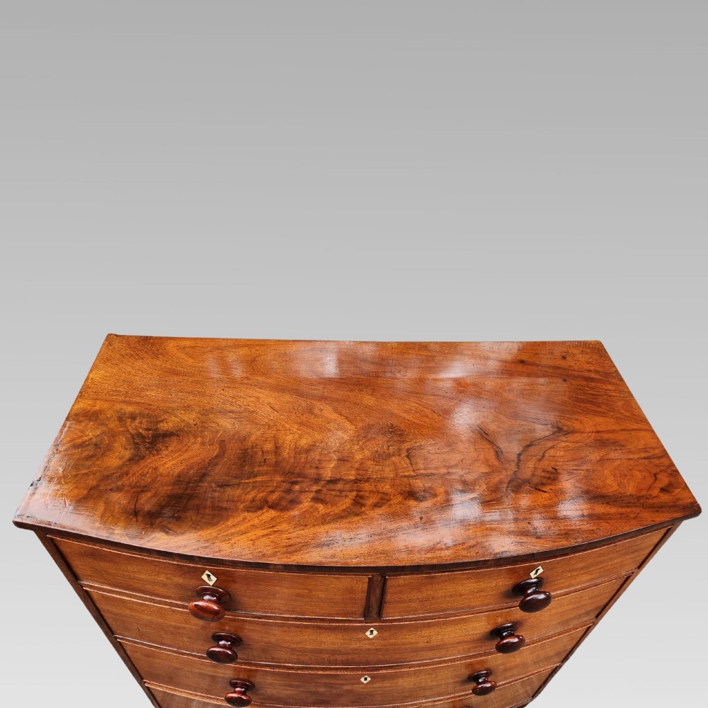 A Victorian mahogany bow-front chest of drawers featuring two short drawers over three long drawers with dark turned handles and turned feet. View XIV