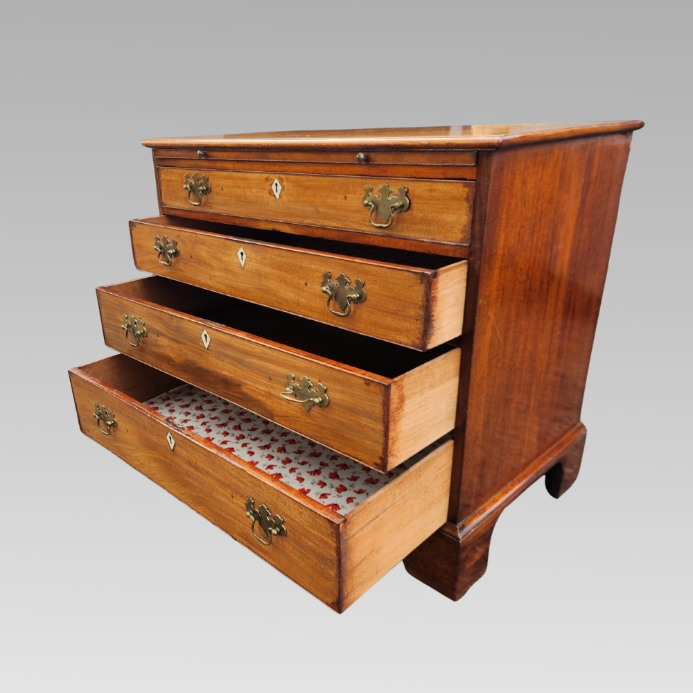 A Georgian mahogany chest of drawers featuring four graduated drawers with brass batwing handles, keyhole escutcheons, a brushing slide, and bracket feet. View V