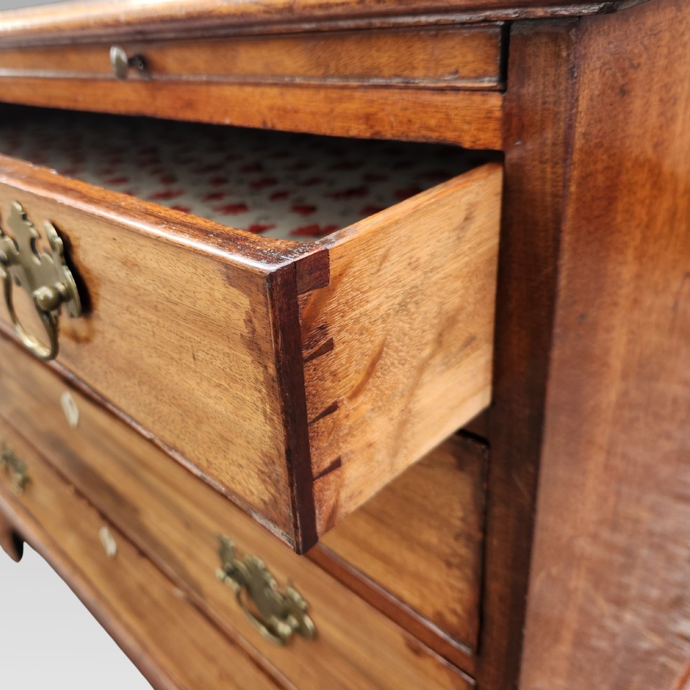 A Georgian mahogany chest of drawers featuring four graduated drawers with brass batwing handles, keyhole escutcheons, a brushing slide, and bracket feet. View VI