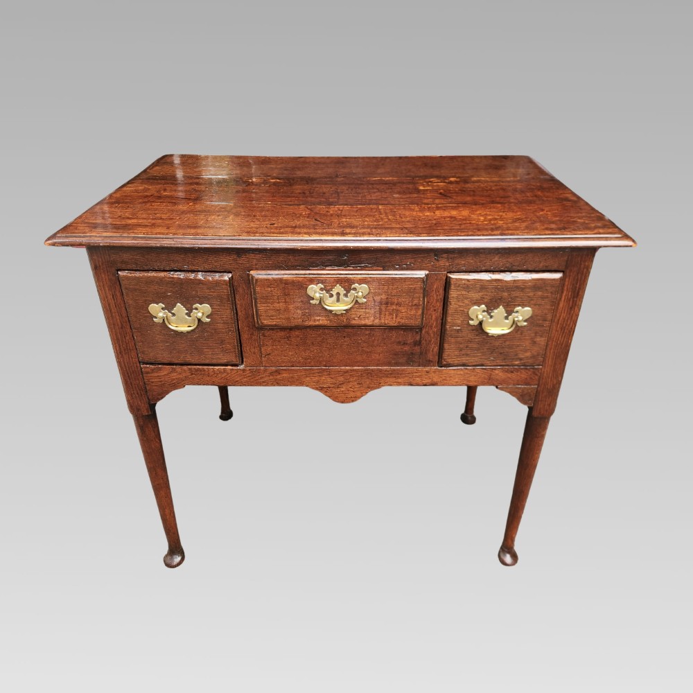 An antique Georgian oak lowboy side table featuring three front drawers with brass handles, a shaped apron, and four slender cabriole legs.