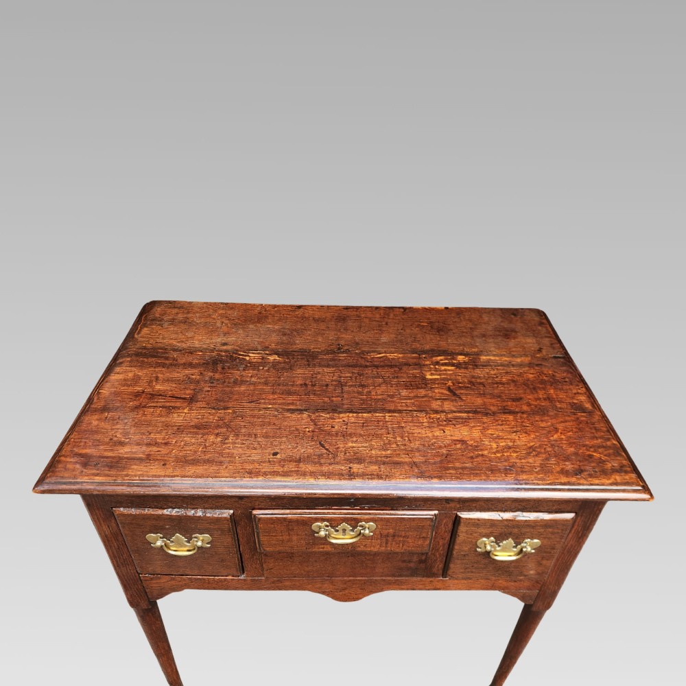 An antique Georgian oak lowboy side table featuring three front drawers with brass handles, a shaped apron, and four slender cabriole legs. View II
