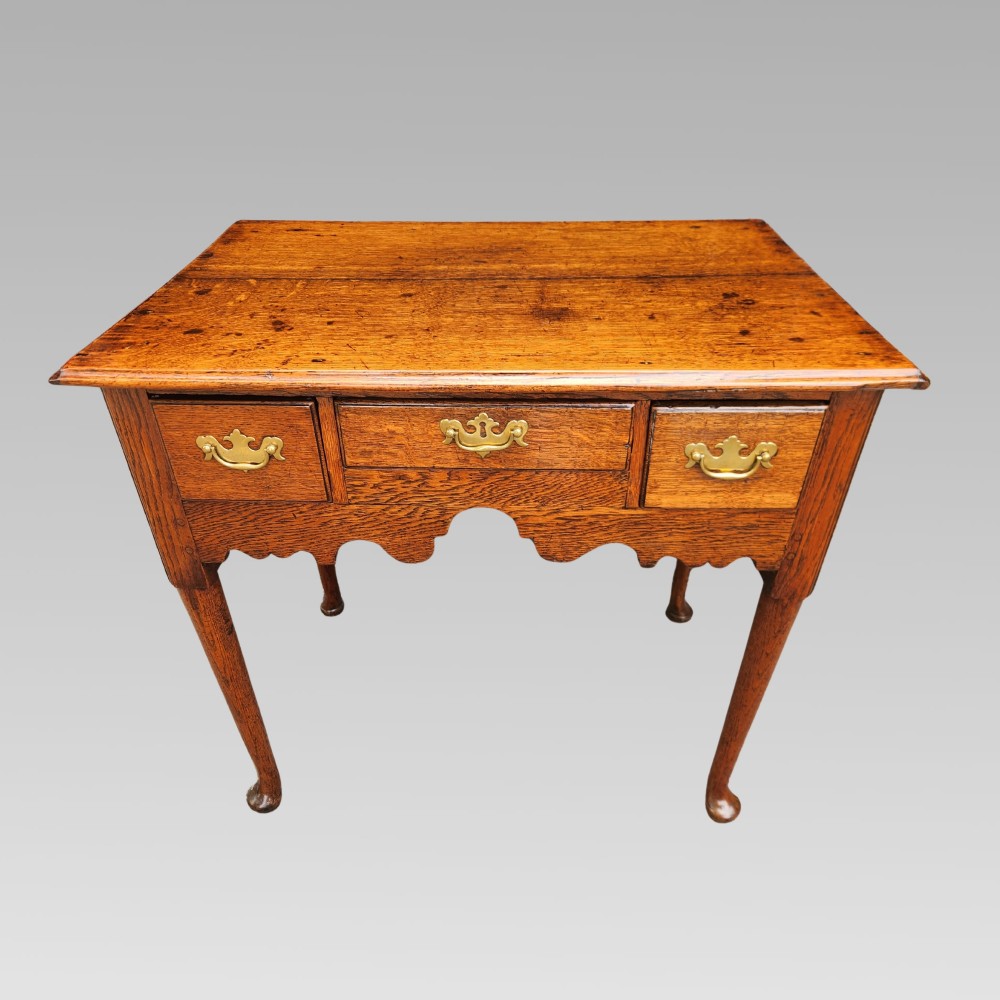 An antique Georgian oak lowboy side table featuring three drawers with brass handles, a shaped apron, and cabriole legs on pad feet.
