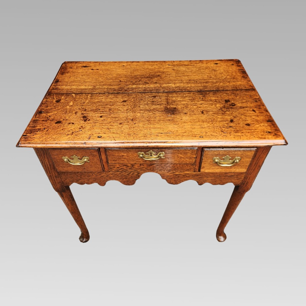 An antique Georgian oak lowboy side table featuring three drawers with brass handles, a shaped apron, and cabriole legs on pad feet. View II