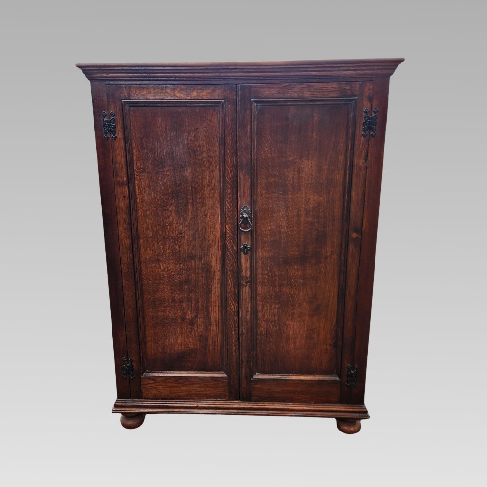 A dark brown Victorian English oak double-door storage cupboard with decorative black iron hinges and bun feet. View II