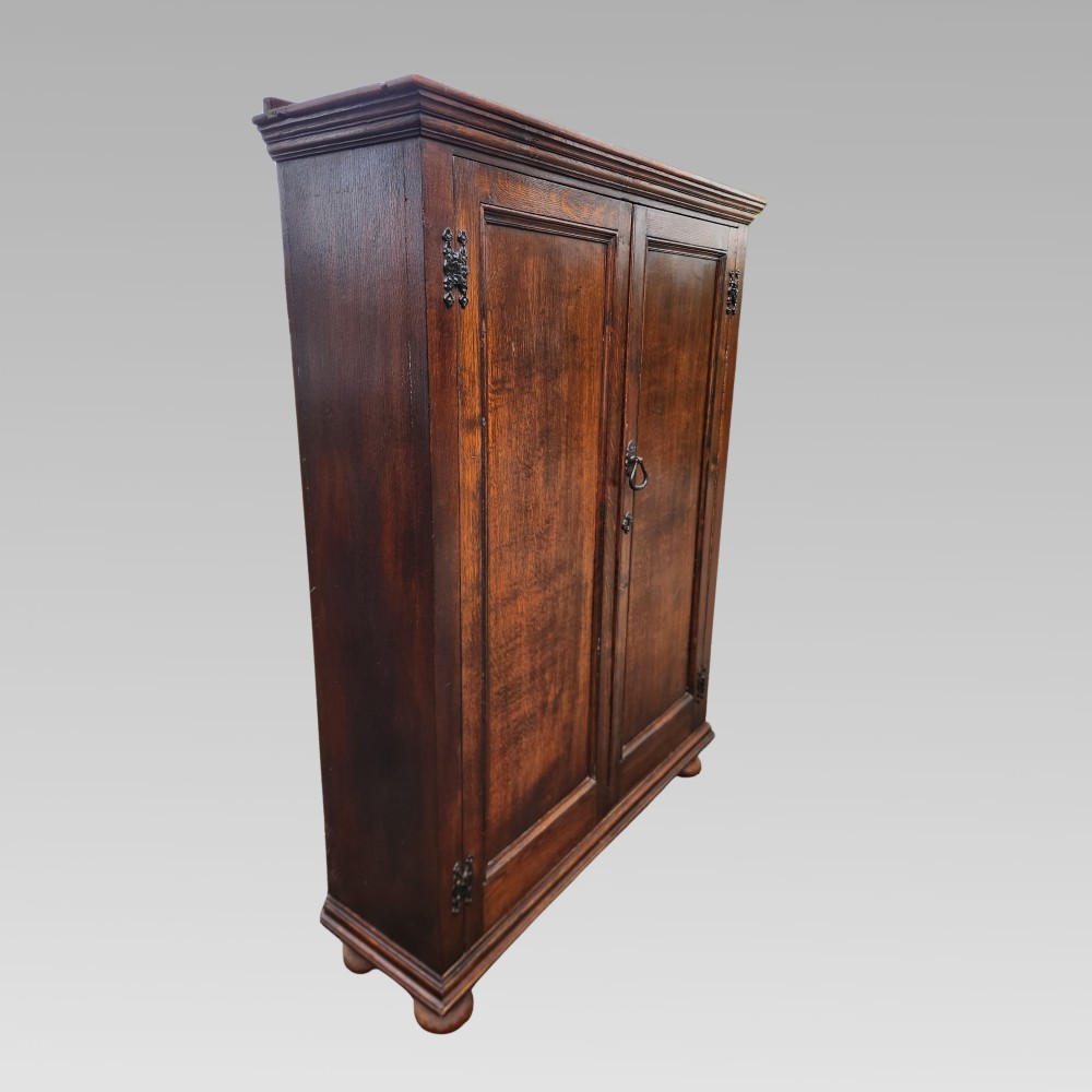 A dark brown Victorian English oak double-door storage cupboard with decorative black iron hinges and bun feet. View III