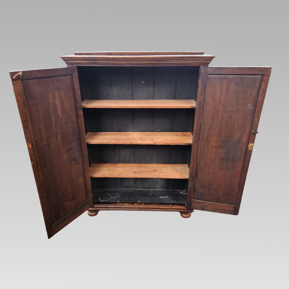 A dark brown Victorian English oak double-door storage cupboard with decorative black iron hinges and bun feet. View IV