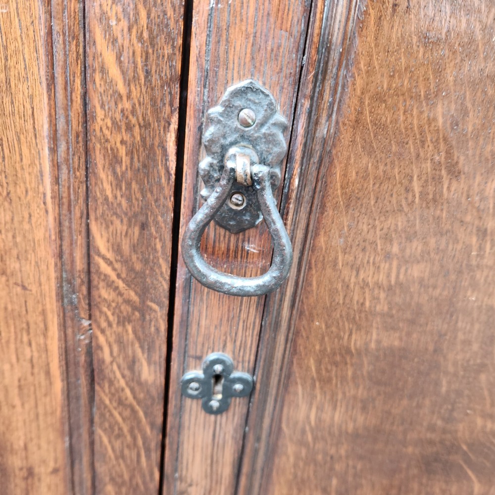 A dark brown Victorian English oak double-door storage cupboard with decorative black iron hinges and bun feet. View V