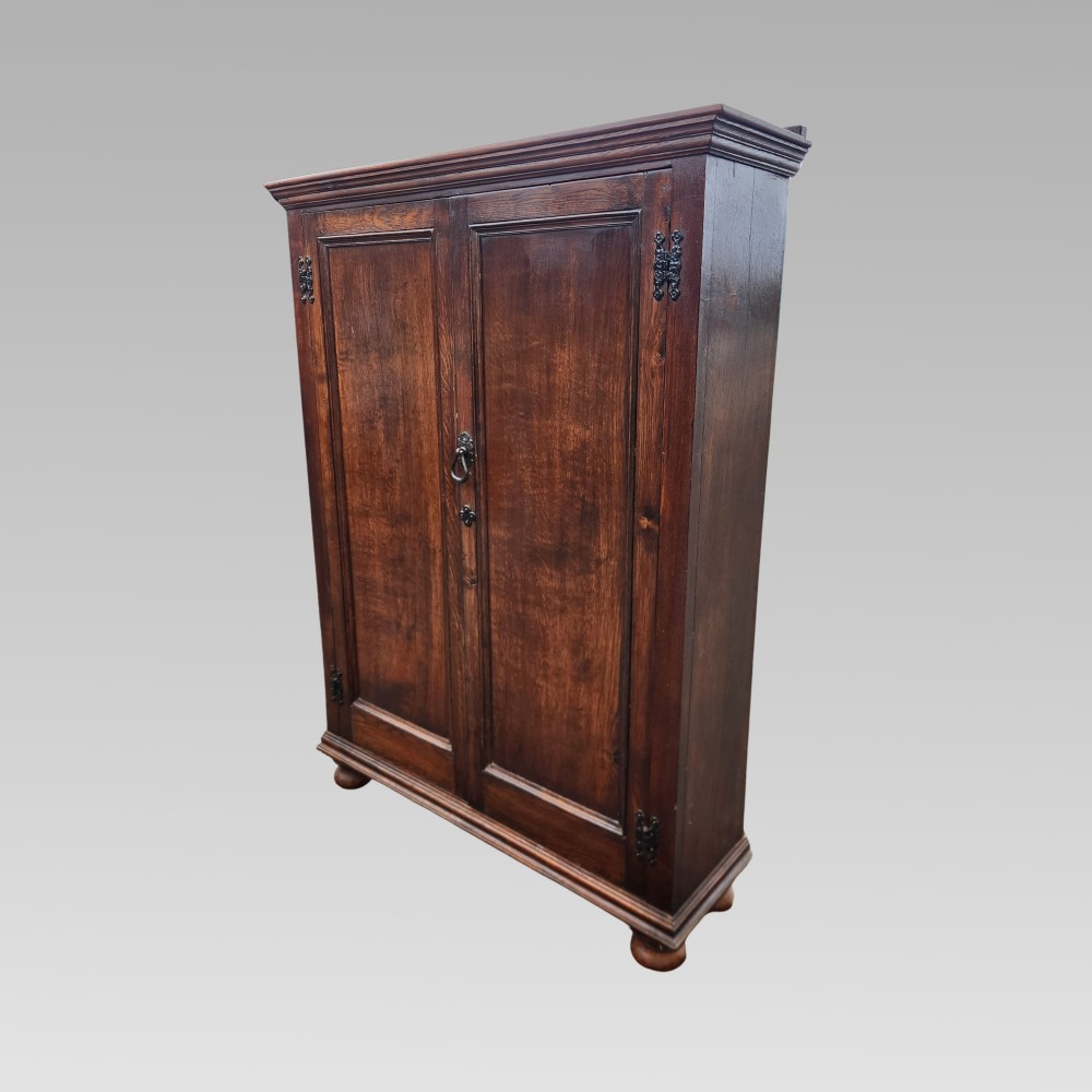 A dark brown Victorian English oak double-door storage cupboard with decorative black iron hinges and bun feet.
