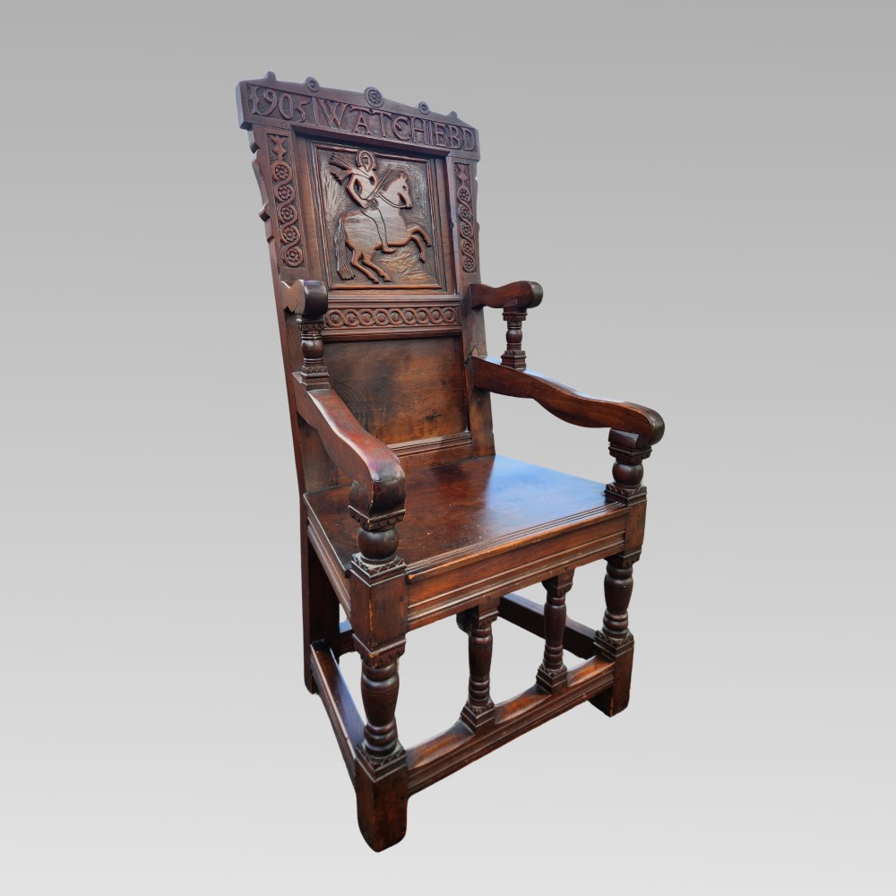 A dark oak wainscot armchair featuring a carved back panel with an equestrian motif, dated cresting rail, and turned legs.