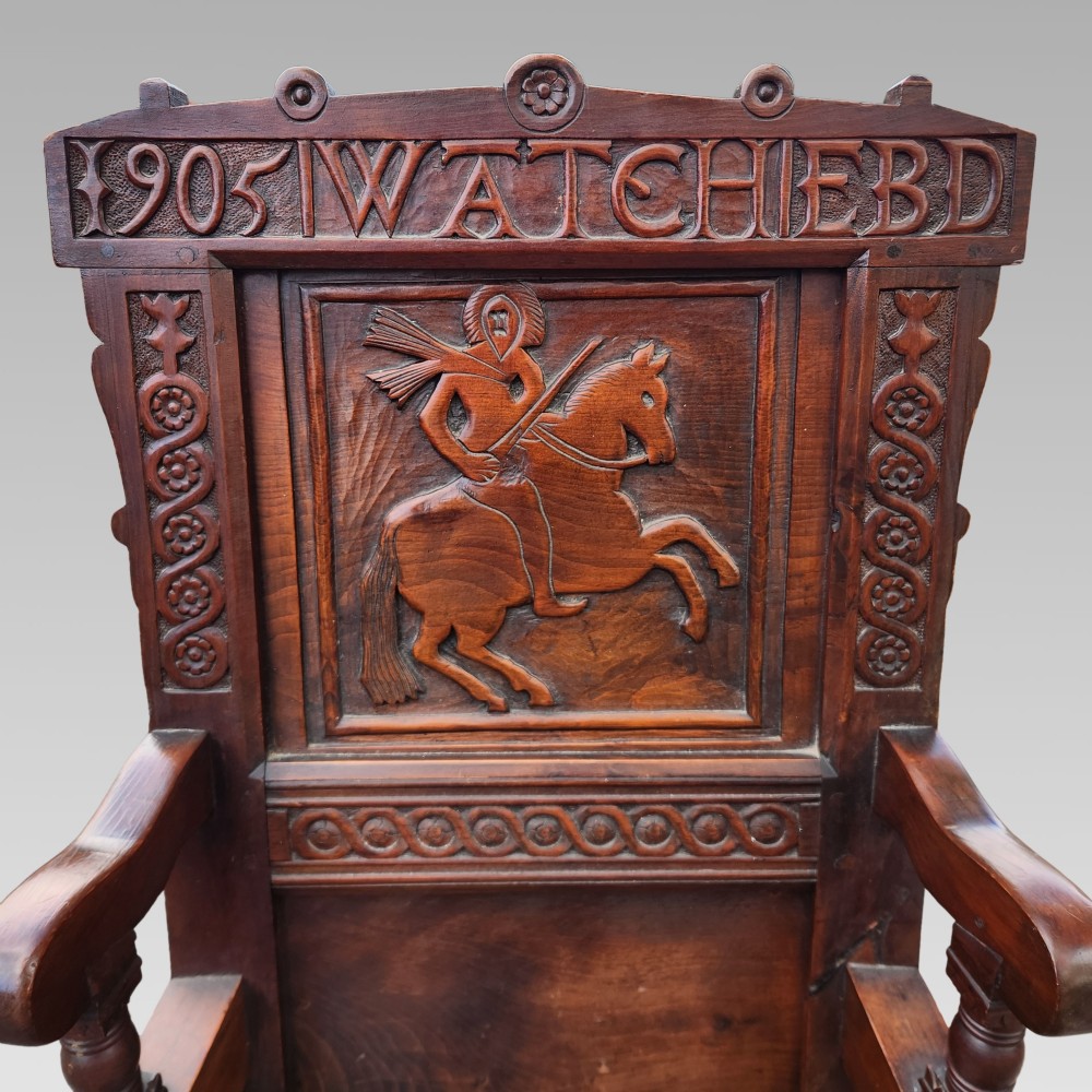 A dark oak wainscot armchair featuring a carved back panel with an equestrian motif, dated cresting rail, and turned legs. View III