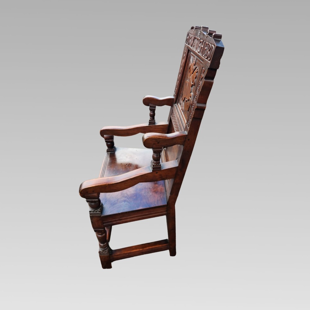 A dark oak wainscot armchair featuring a carved back panel with an equestrian motif, dated cresting rail, and turned legs. View IV