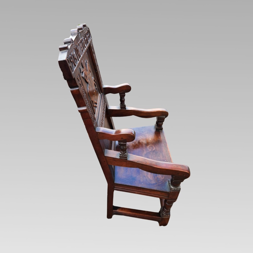 A dark oak wainscot armchair featuring a carved back panel with an equestrian motif, dated cresting rail, and turned legs. View V