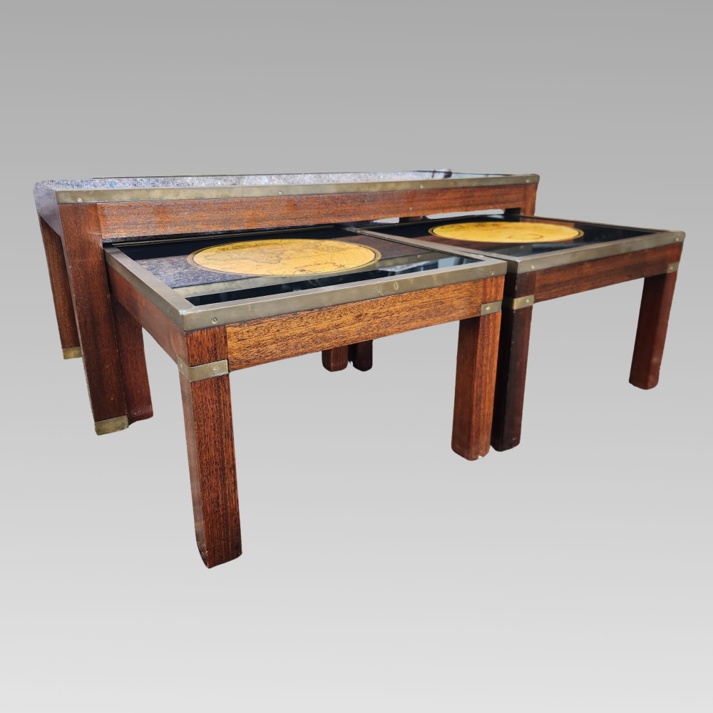 A dark mahogany campaign style nest of three coffee tables featuring glass tops with inset world map illustrations and brass corner mounts. View II