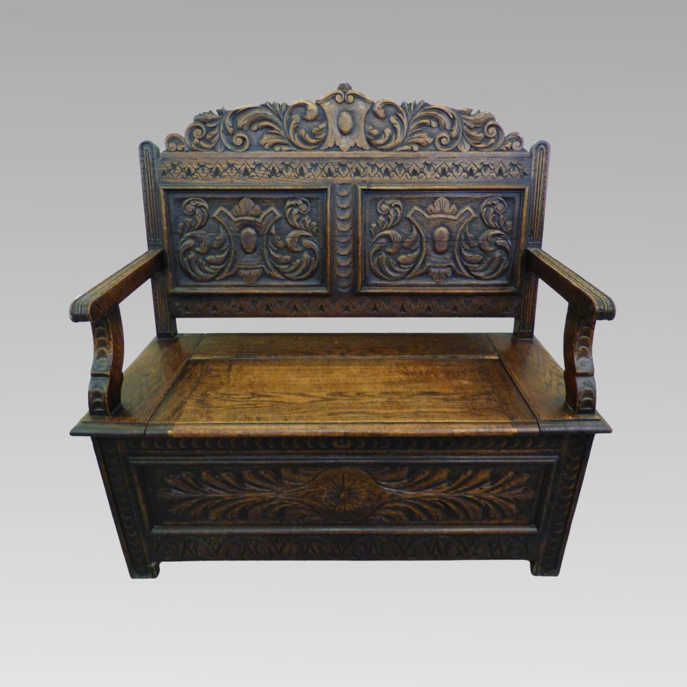 Carved dark oak hall settle featuring a cresting rail, panelled back, curved armrests, and a hinged storage seat.