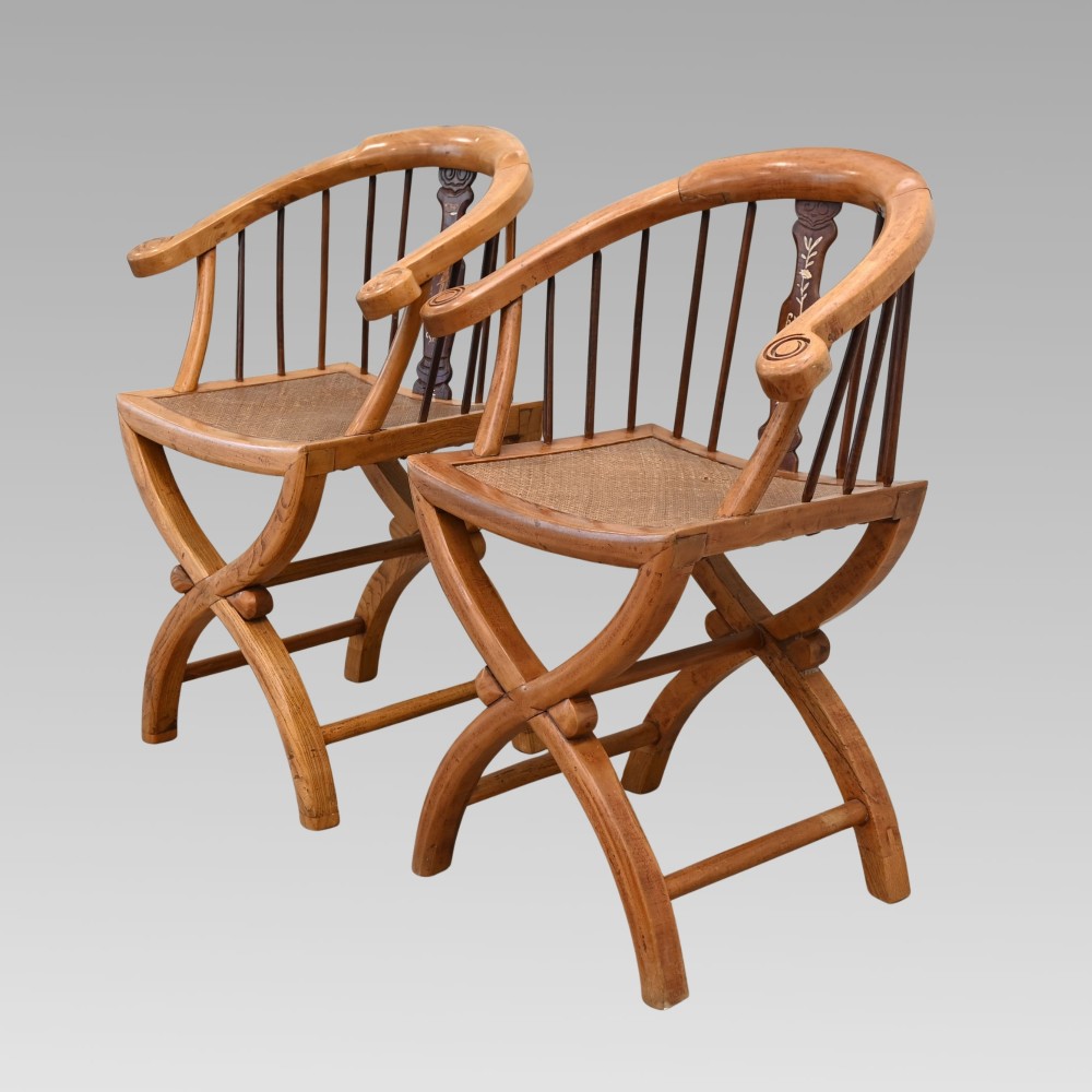 A pair of Chinese fruitwood horseshoe chairs featuring curved crest rails, vertical spindles, woven cane seats, cross-framed legs, and central carved splats with bone inlay.