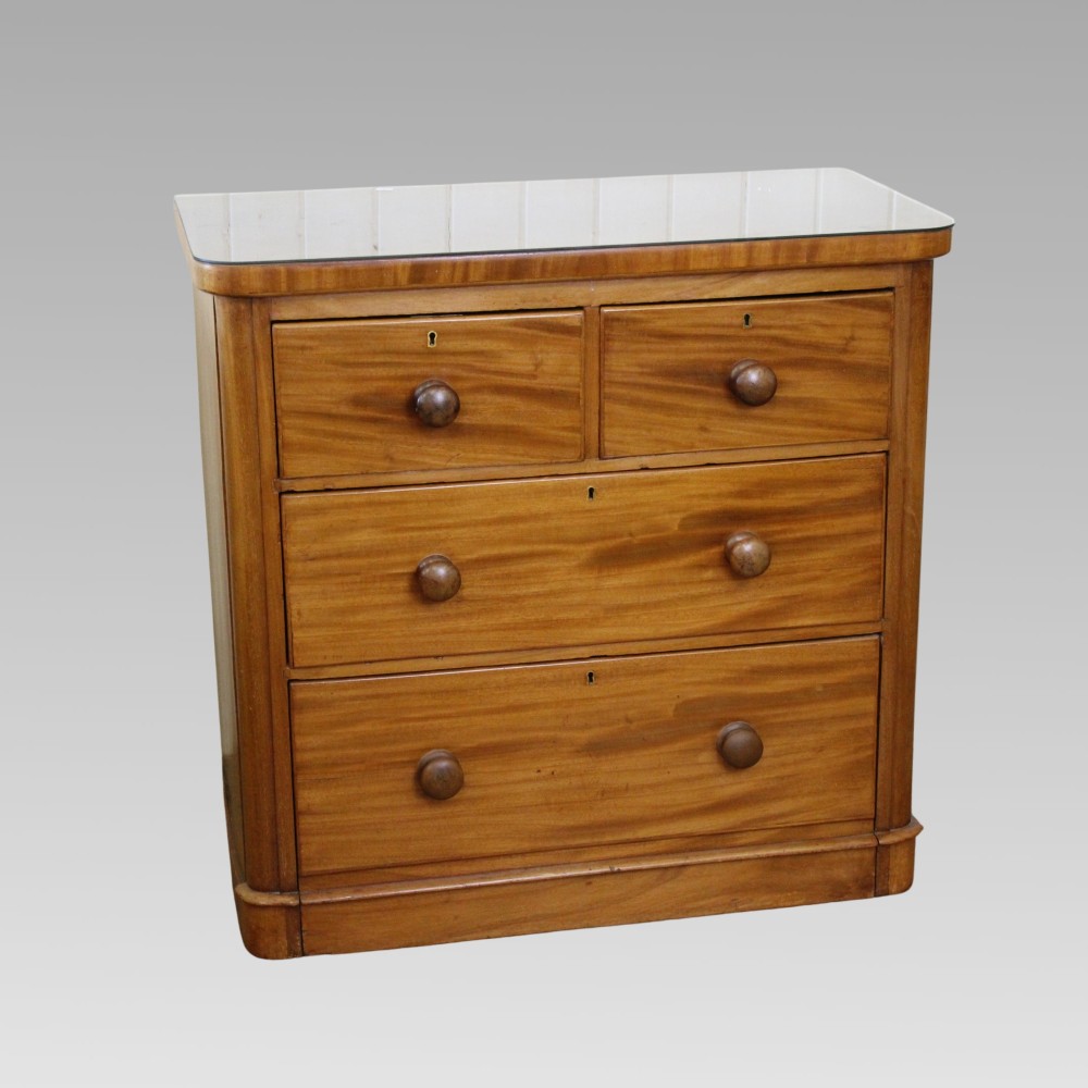 A Victorian flame mahogany chest of drawers featuring a two over two drawer layout, turned wooden knobs, brass escutcheons, and rounded front corners.