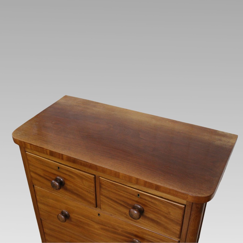 A Victorian flame mahogany chest of drawers featuring a two over two drawer layout, turned wooden knobs, brass escutcheons, and rounded front corners. View II
