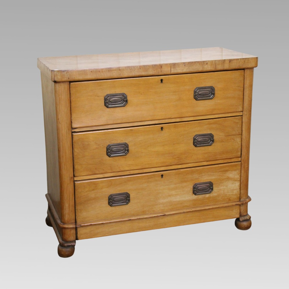 A Victorian light pine chest of drawers featuring three full-width drawers with brass recessed handle plates and turned bun feet.