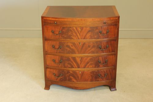 fig 1. An early 20th-century mahogany bow-fronted bachelors chest of drawers featuring four graduated drawers, a top brushing slide, flame mahogany veneer, and brass handles.
