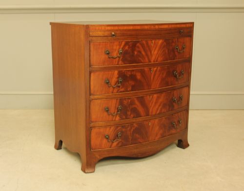 fig 2. An early 20th-century mahogany bow-fronted bachelors chest of drawers featuring four graduated drawers, a top brushing slide, flame mahogany veneer, and brass handles.