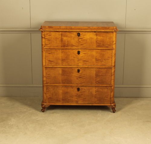 fig 4. A 19th-century Swedish chest of drawers crafted from flame birch veneer with four horizontal drawers, central dark escutcheons, and short carved bracket feet.