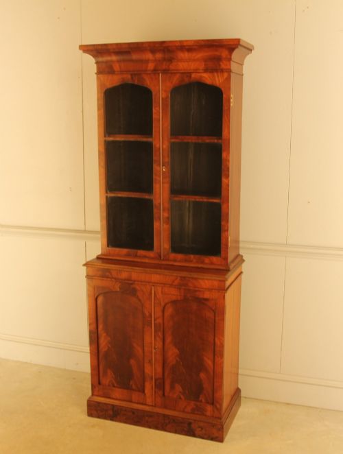 fig 2. A two-door 19th-century mahogany bookcase featuring an upper glazed display section with internal shelves above a lower cabinet with flame mahogany panelled doors.