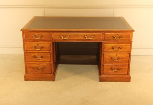 fig 1. An early 20th-century golden oak twin-pedestal bankers desk featuring a dark leather inset top, nine drawers with brass handles, and panelled sides.