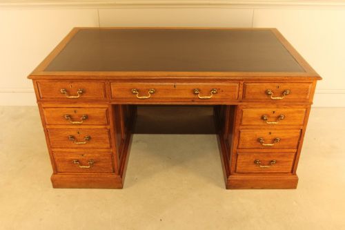 fig 2. An early 20th-century golden oak twin-pedestal bankers desk featuring a dark leather inset top, nine drawers with brass handles, and panelled sides.