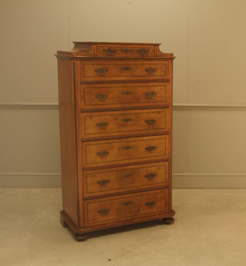 fig 1. A tall 19th-century Swedish burr walnut chest of drawers featuring seven drawers, crossbanded inlay, ornate brass handles, and a stepped top section.