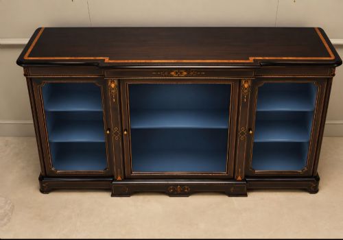 fig 1. A Victorian ebonised wood breakfront display cabinet featuring three glazed doors, gold inlay detail, and a blue painted interior.