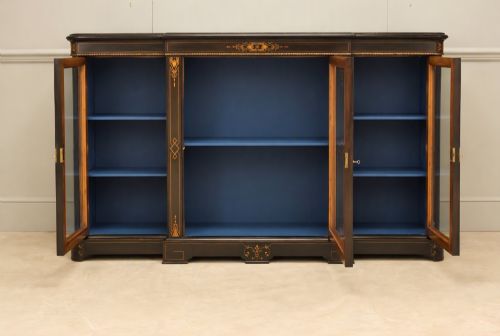fig 2. A Victorian ebonised wood breakfront display cabinet featuring three glazed doors, gold inlay detail, and a blue painted interior.