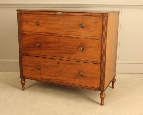fig 2. A Regency mahogany chest of drawers featuring three graduated drawers with brass turned knobs and reeded side pilasters resting on turned feet.