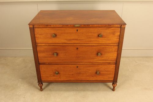 fig 3. A Regency mahogany chest of drawers featuring three graduated drawers with brass turned knobs and reeded side pilasters resting on turned feet.