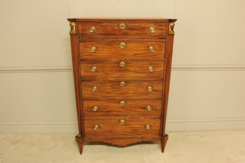 fig 1. A French 19th-century mahogany tallboy chest of drawers featuring six drawers, brass ring handles, escutcheons, and fluted side pilasters topped with brass busts.