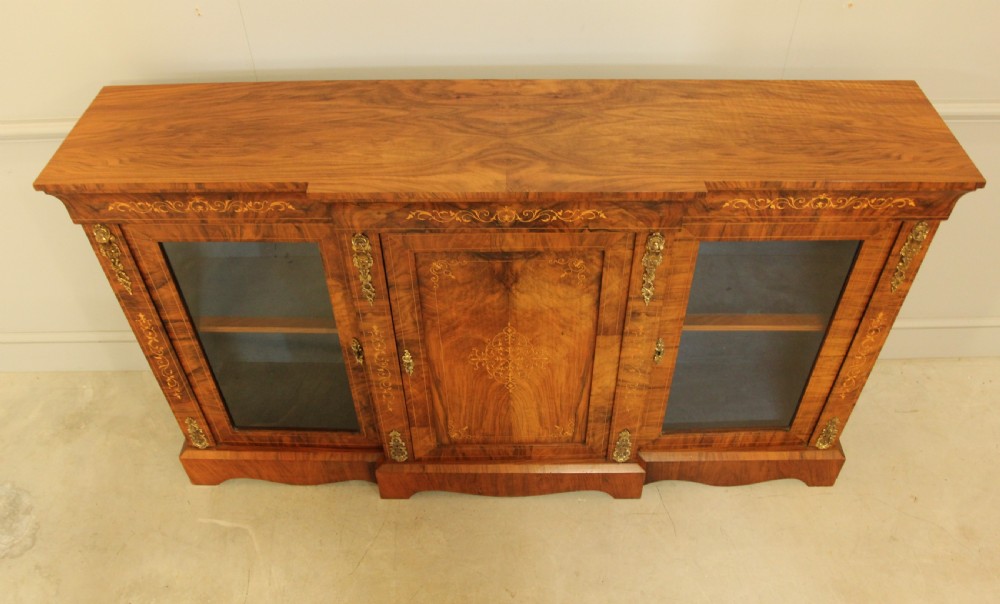 A Victorian low breakfront credenza crafted from burr walnut with marquetry inlay, gilt-brass mounts, a central panelled door, and two outer glazed doors. View V