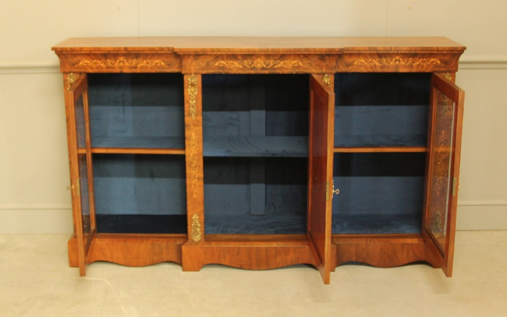 A Victorian low breakfront credenza crafted from burr walnut with marquetry inlay, gilt-brass mounts, a central panelled door, and two outer glazed doors. View VI