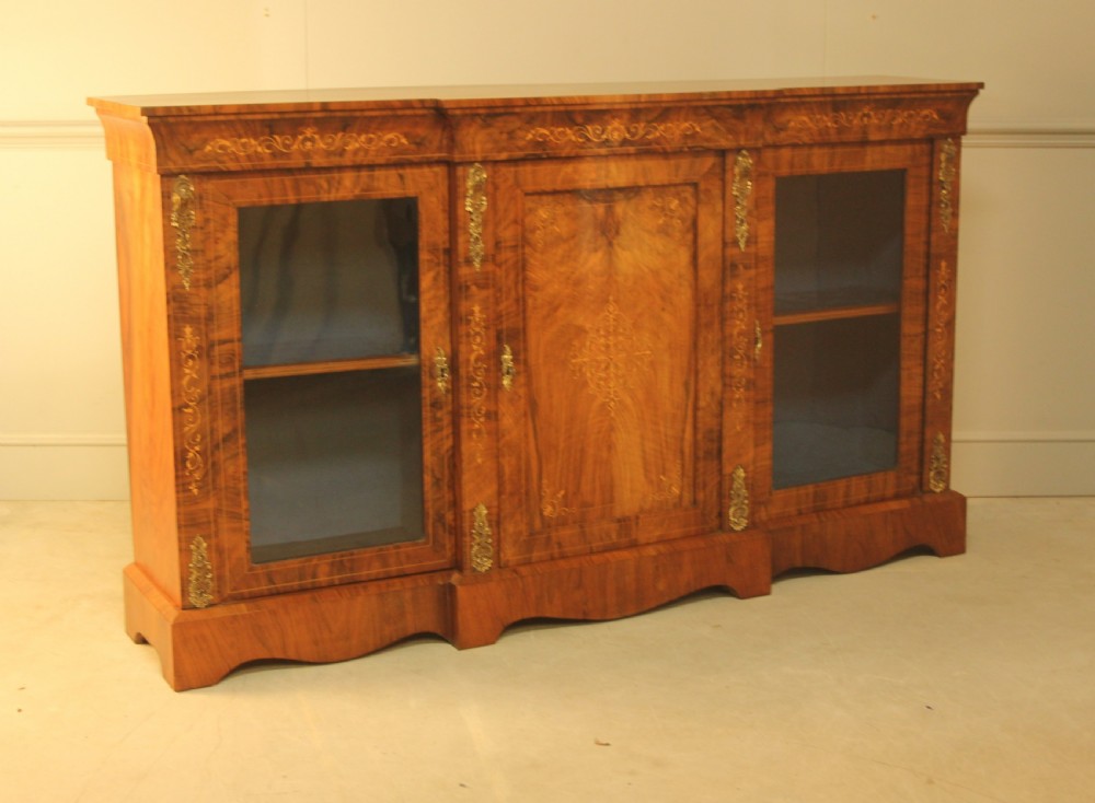 A Victorian low breakfront credenza crafted from burr walnut with marquetry inlay, gilt-brass mounts, a central panelled door, and two outer glazed doors. View VII
