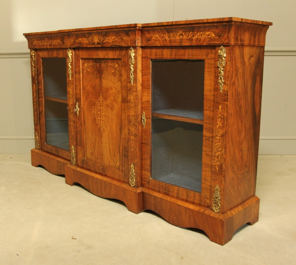 A Victorian low breakfront credenza crafted from burr walnut with marquetry inlay, gilt-brass mounts, a central panelled door, and two outer glazed doors. View VIII