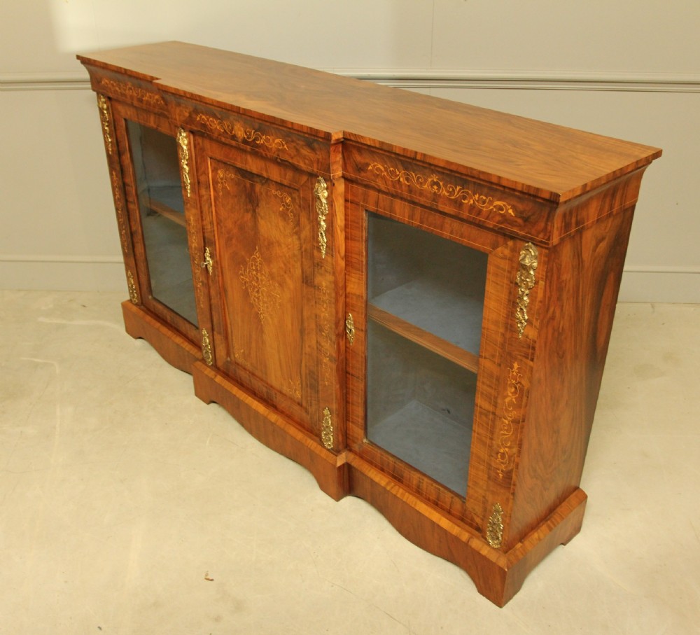 A Victorian low breakfront credenza crafted from burr walnut with marquetry inlay, gilt-brass mounts, a central panelled door, and two outer glazed doors. View IX