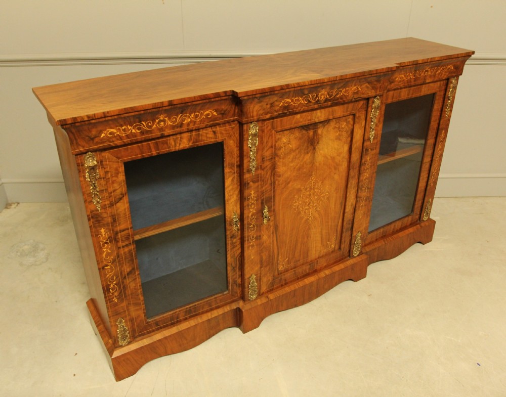 A Victorian low breakfront credenza crafted from burr walnut with marquetry inlay, gilt-brass mounts, a central panelled door, and two outer glazed doors. View X