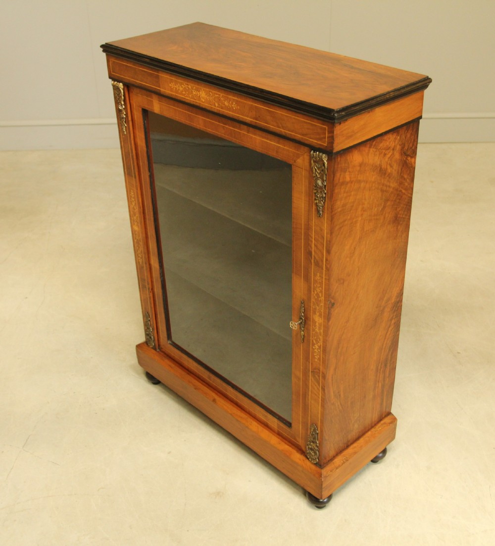 A Victorian walnut pier display cabinet featuring a single glazed door, floral marquetry inlay, decorative brass mounts, and turned feet. View II