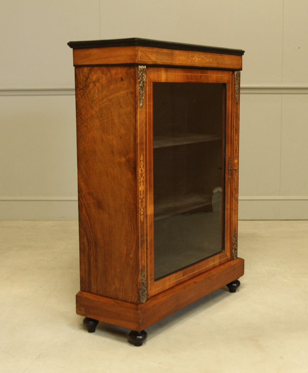 A Victorian walnut pier display cabinet featuring a single glazed door, floral marquetry inlay, decorative brass mounts, and turned feet. View III