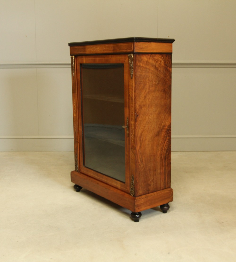 A Victorian walnut pier display cabinet featuring a single glazed door, floral marquetry inlay, decorative brass mounts, and turned feet. View VIII