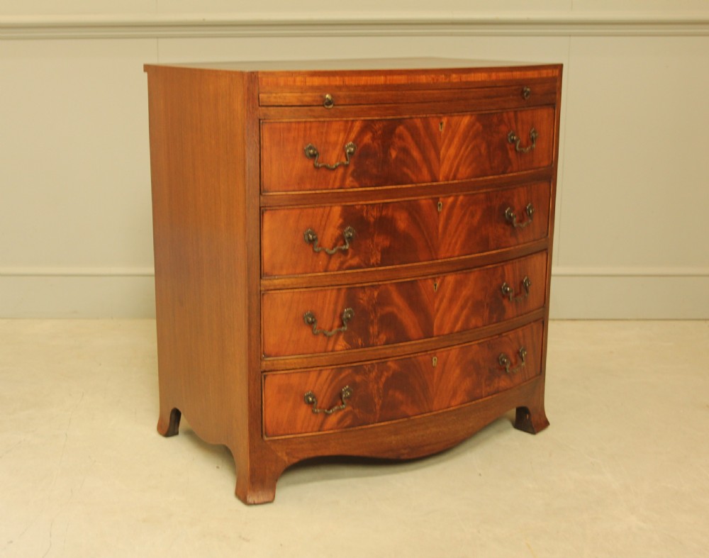 An early 20th-century mahogany bow-fronted bachelors chest of drawers featuring four graduated drawers, a top brushing slide, flame mahogany veneer, and brass handles. View III